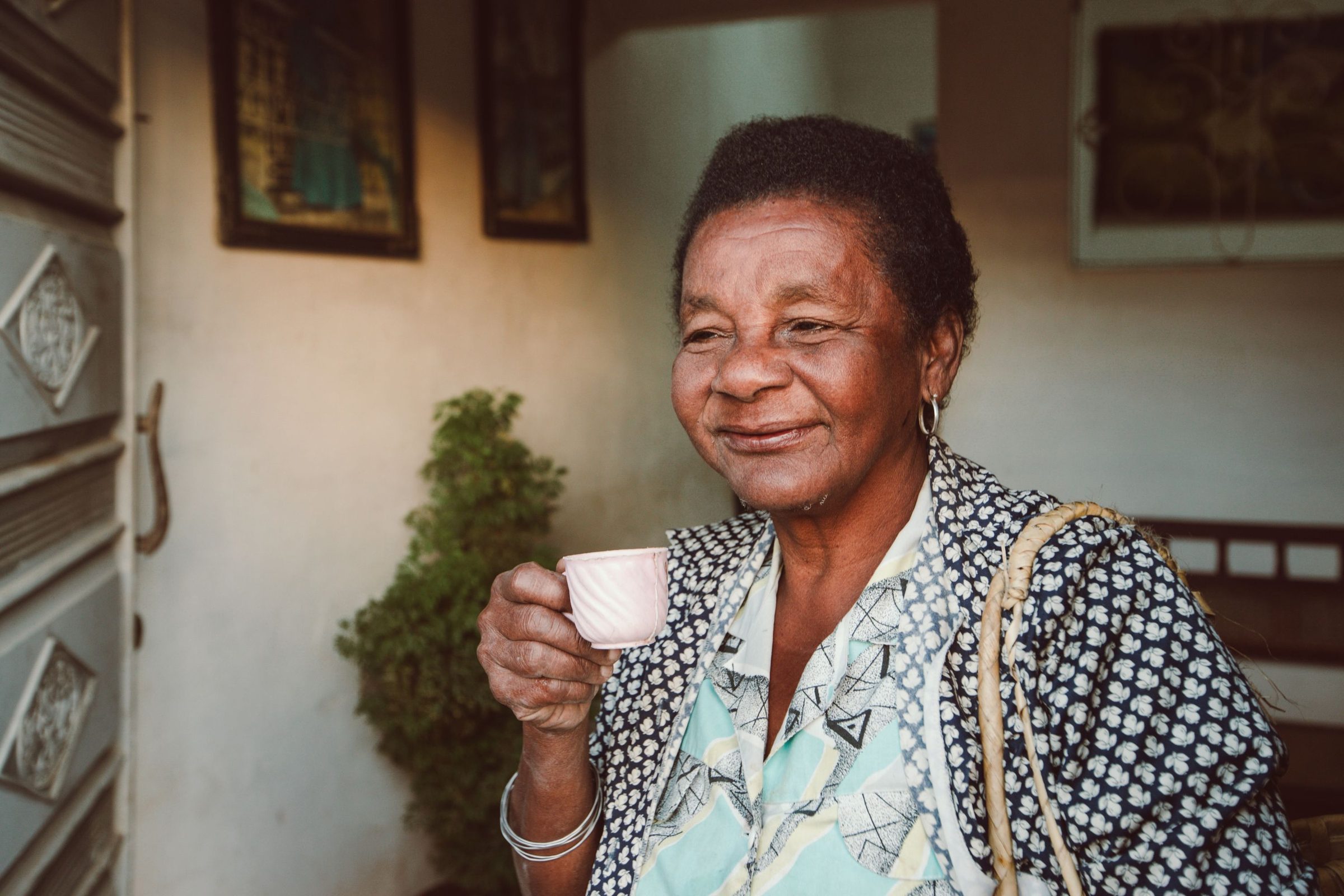 An older woman smiling as she drinks a cup of coffee