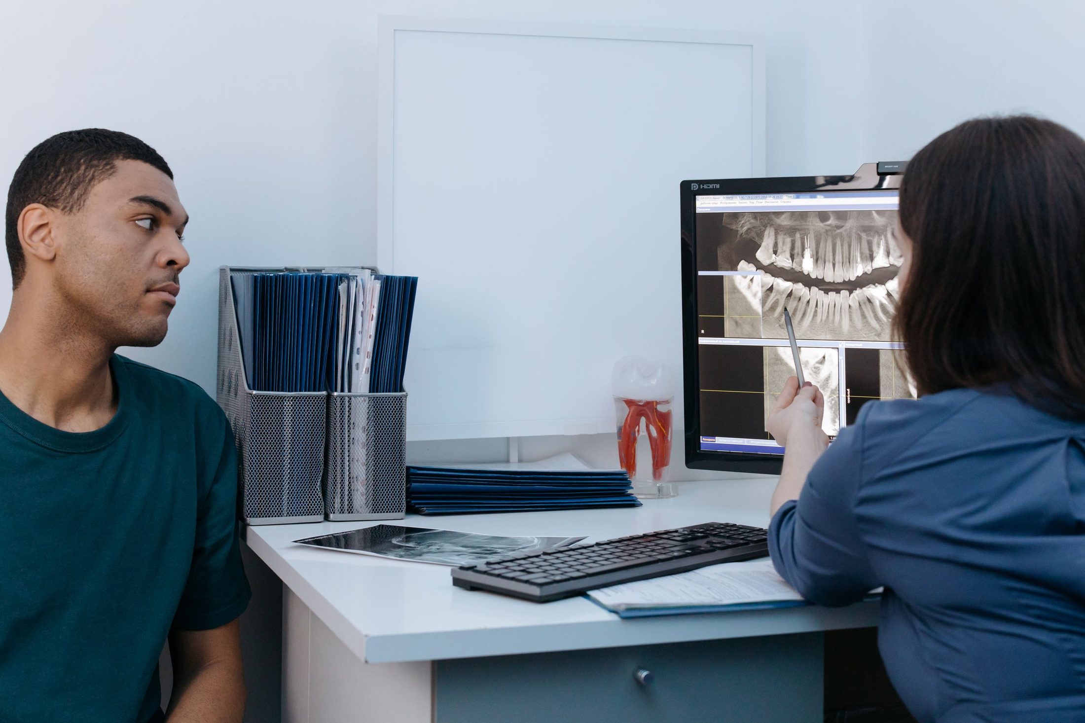 A dentist reviewing a panoramic X-ray on screen with a patient