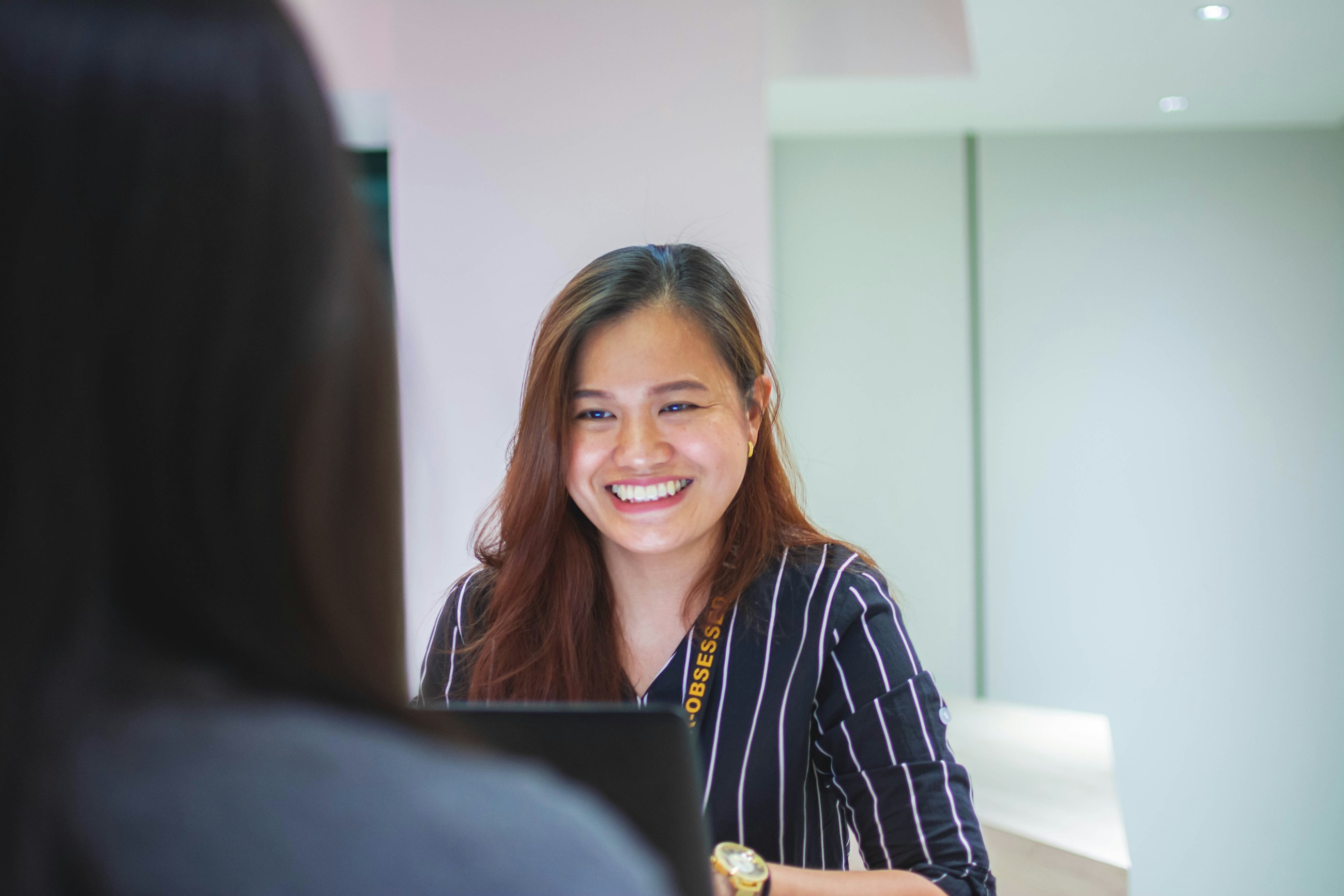 A smiling front-desk coordinator helping a patient at the desk