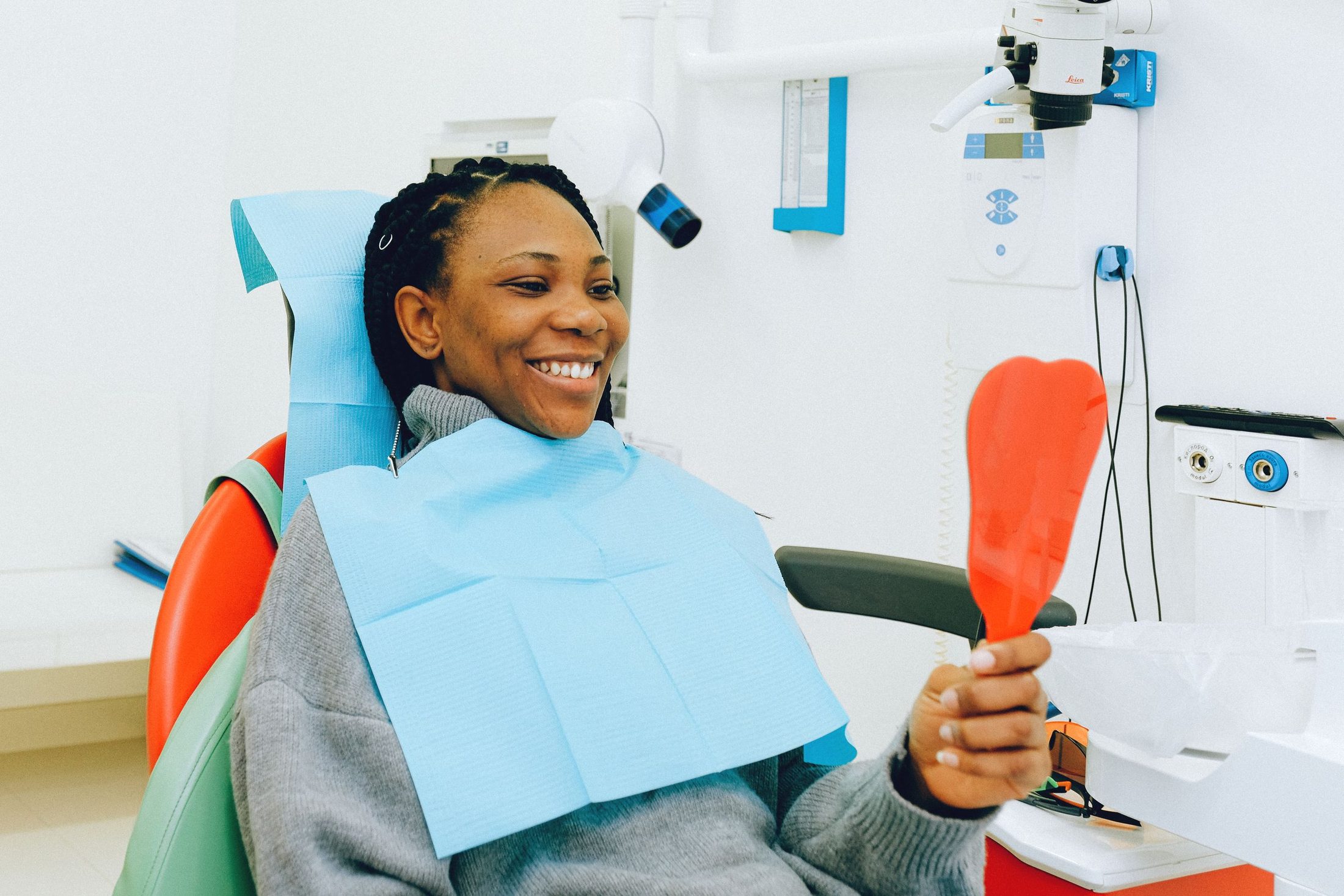 A smiling woman in a dental chair looking at her teeth in a hand mirror